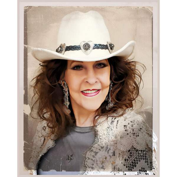 Donna Fargo wearing a white hat and lace vest smiling in her new promotional photo.