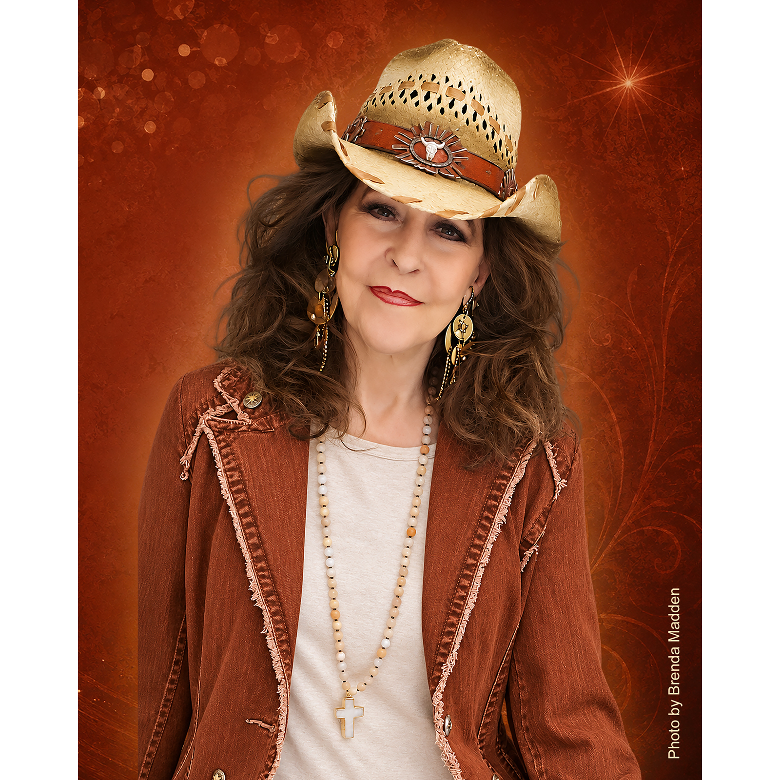 Donna Fargo wearing a straw cowboy hat, rust-colored jacket, and cross necklace against a warm, textured rust-orange background with sparkling accents.