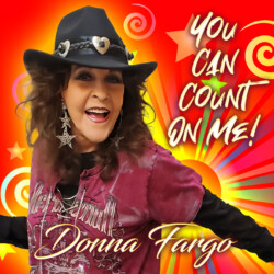 Donna Fargo smiling warmly, holding a microphone, radiating confidence and joy as she promotes her new single “You Can Count on Me.”